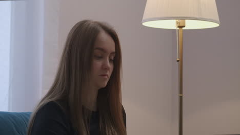 pretty-woman-with-long-hair-is-resting-in-living-room-of-apartment-switching-off-lights-of-floor-lamp-closeup-portrait-in-modern-home